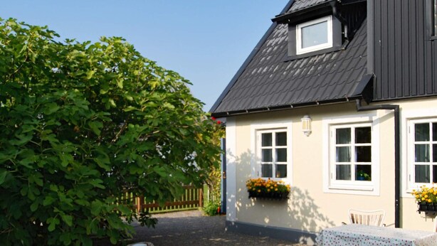 A house with a sloped roof, white exterior walls, and a gravel driveway. There is a table with a white tablecloth and chairs outside the house. - 4 Star Holiday Home in Smygehamn (Trelleborg)