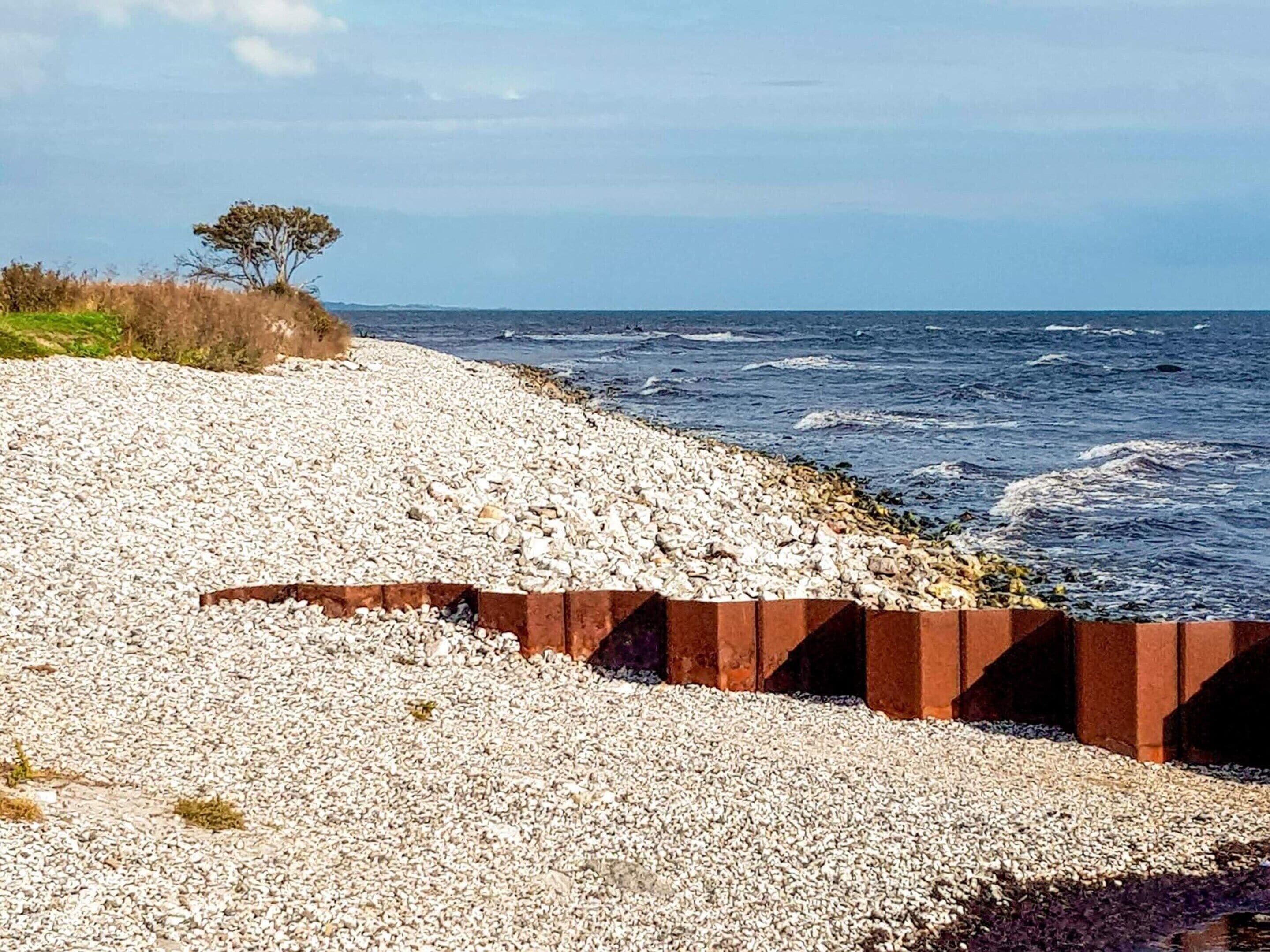 A pebble beach with a rocky barrier and a tree in the background.