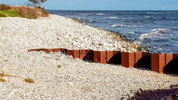 A pebble beach with a rocky barrier and a tree in the background. - 4 Star Holiday Home in Smygehamn (Trelleborg)
