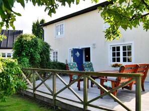 A wooden deck with a table and chairs, a blue door, and a white building with windows. - 5 Person Holiday Home in Smygehamn (Trelleborg)