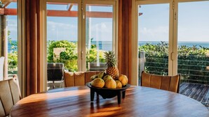 Ein Esstisch mit Obstschale in einem Zimmer mit großen Fenstern und Blick auf das Meer.