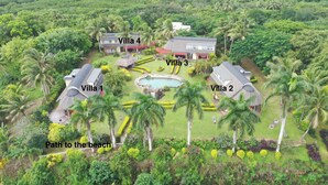 Ein Luftbild eines Resorts mit vier Villen, einem Schwimmbecken und einem Weg zum Strand.