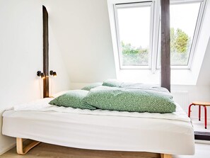 A bedroom with a bed, pillows, a nightstand, a window, and a red stool.