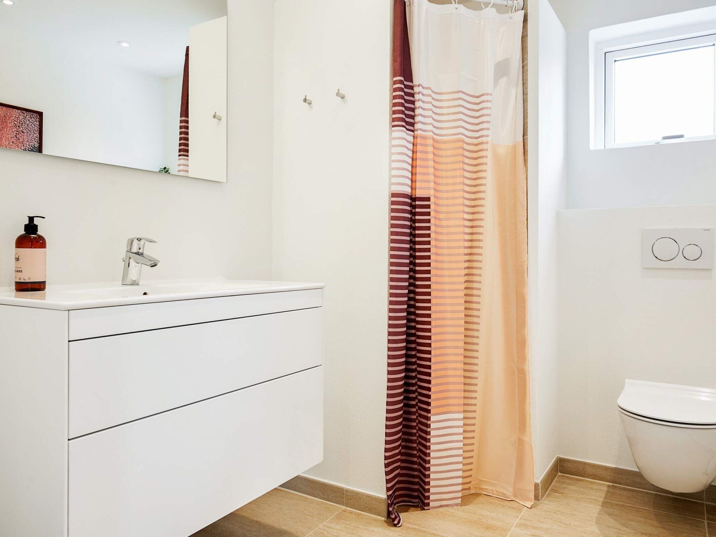 Une salle de bain avec un lavabo blanc, un miroir, un rideau de douche et des toilettes.
