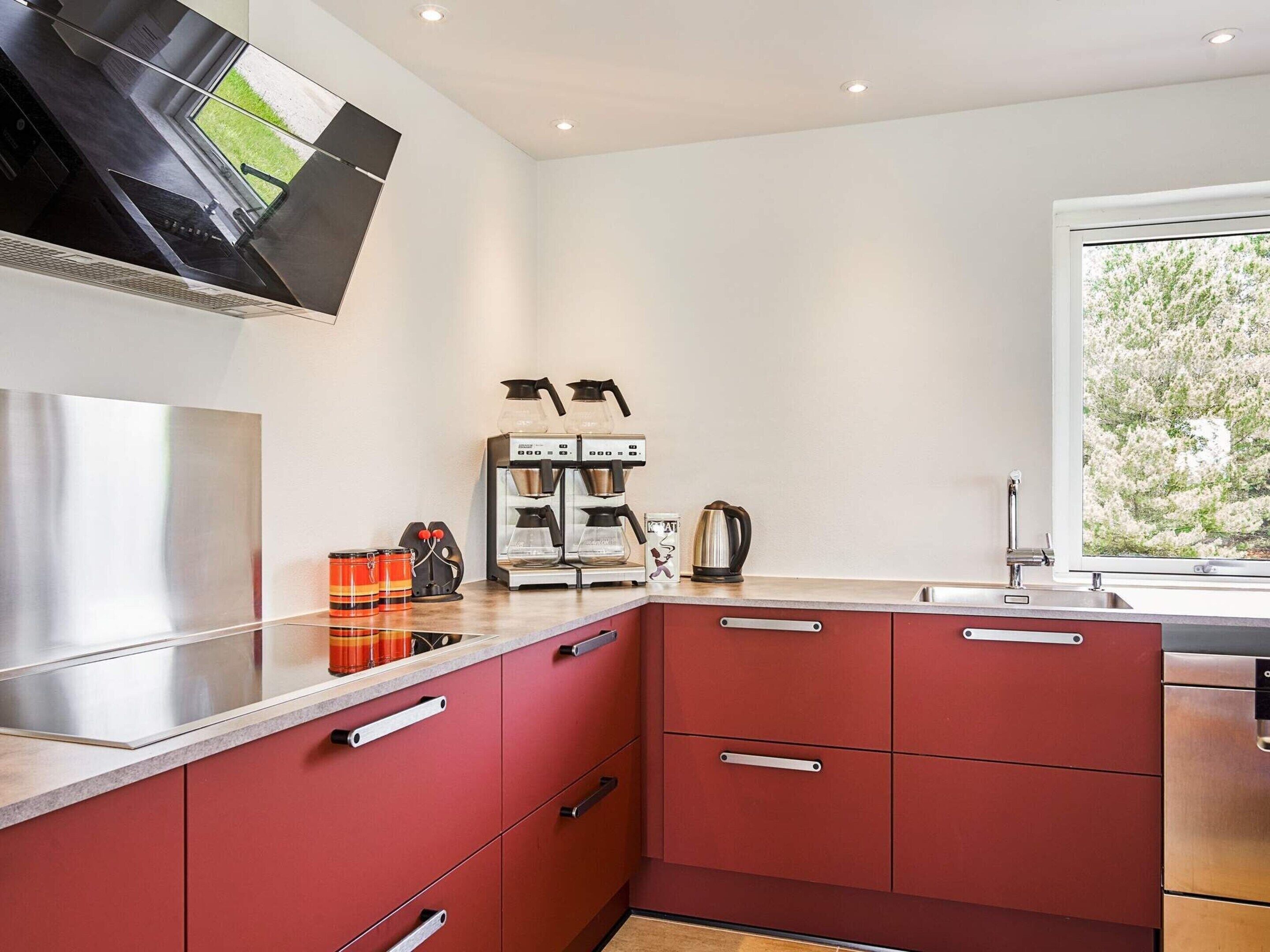 A modern kitchen with red cabinets, a stainless steel countertop, and a coffee machine.