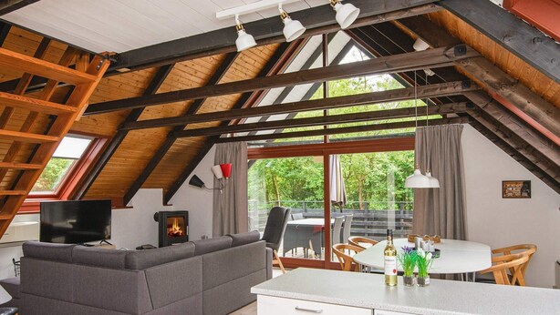 A cozy loft-style room with a wooden ceiling, a fireplace, a sofa, a dining table, and a kitchen area. - 6 Person Holiday Home in Toftlund (Toftlund)