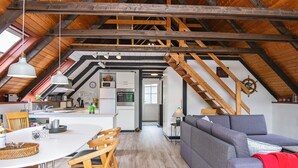 A spacious loft with exposed wooden beams, a kitchen with modern appliances, a dining area with a white table and wooden chairs, and a gray sofa in a cozy living space. - 6 Person Holiday Home in Toftlund (Toftlund)