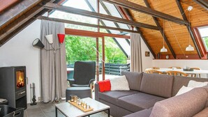 A cozy living room with a fireplace, a sofa, a dining table, and a view of greenery outside. - 6 Person Holiday Home in Toftlund (Toftlund)