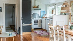 A kitchen with white cabinets, a stove, and a window. There is a dining table with chairs and a rug. - 6 Person Holiday Home in Lokken (Lokken)