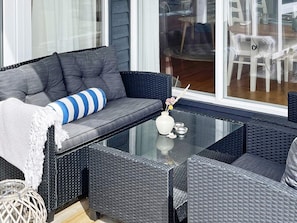 A modern outdoor seating area with a grey sofa, a glass-top table, and wicker furniture. - 6 Person Holiday Home in Lokken (Lokken)