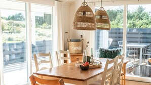 A dining area with a wooden table, white chairs, and wicker pendant lights. - 6 Person Holiday Home in Lokken (Lokken)