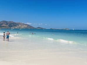 A beach with clear turquoise water, people swimming and sunbathing, and boats in the distance. - Waterfront in Baie Orientale. Design. Large pool. Private water tank. (Collectivité de Saint-Martin)