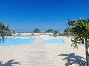 A pool area with two swimming pools, a wooden walkway, and palm trees.