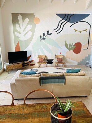 Ein Wohnzimmer mit einer Couch, zwei Beistelltischen, einem Fernseher und einem großen, abstrakten Wandbild.