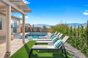 A backyard with a swimming pool, lounge chairs, and a pergola.