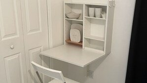 Un bureau blanc avec des étagères, une chaise blanche et un lit avec une literie blanche.