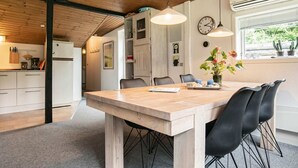 A modern kitchen with a wooden ceiling, a dining area with a wooden table and black chairs, and a window with potted plants. - 6 Person Holiday Home in Blavand (Blavand)