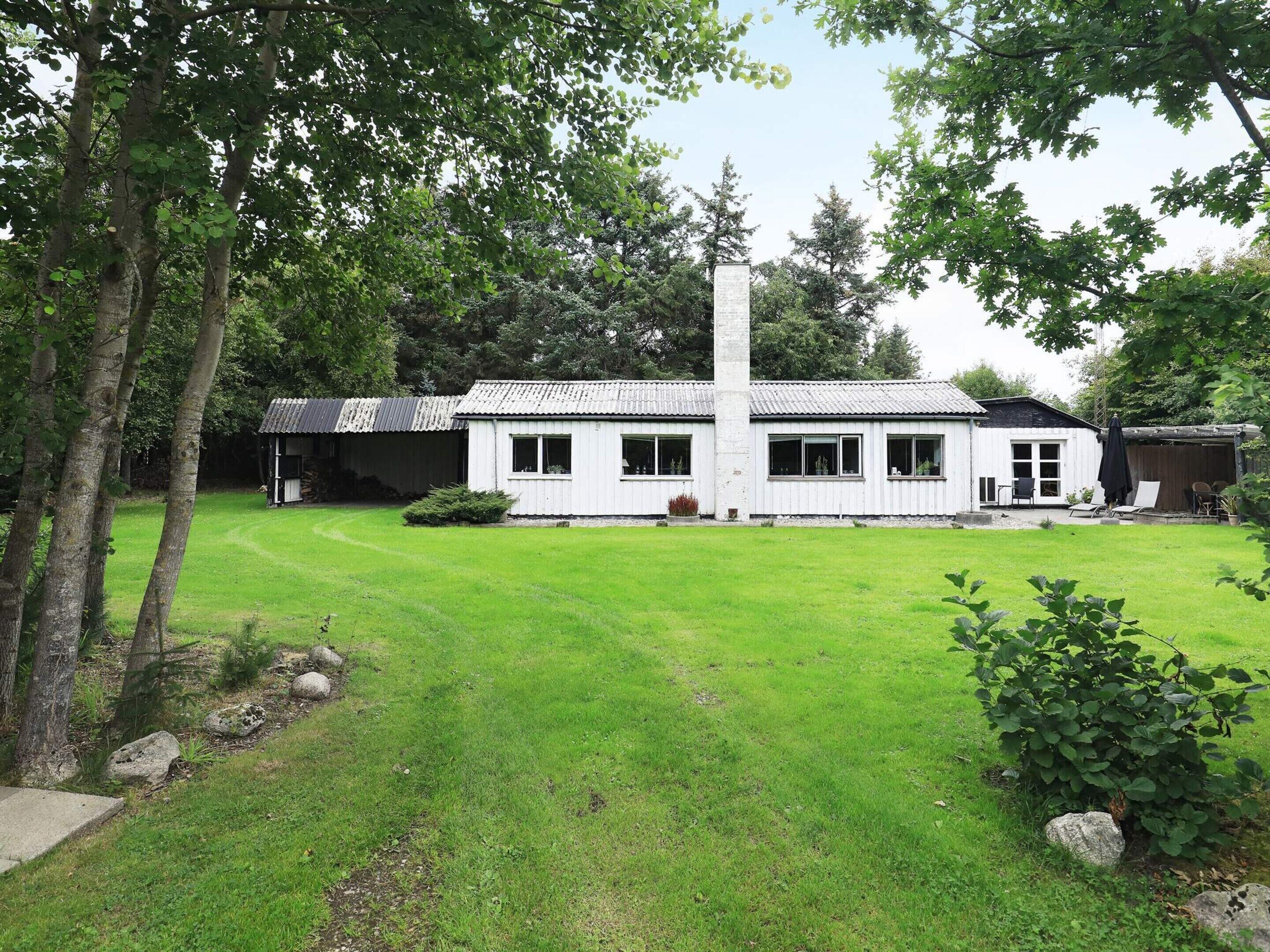 A white building with a tiled roof, a tall chimney, and a well-maintained lawn.