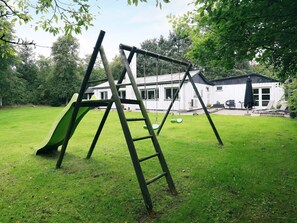 A swing set in a grassy yard with a house in the background. - 6 Person Holiday Home in Blavand (Blavand)