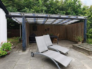 A covered patio area with two lounge chairs, a table, and a grill. - 6 Person Holiday Home in Blavand (Blavand)