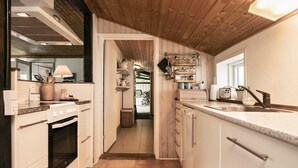 A kitchen with white cabinets, a stove, and a sink. There is a wooden ceiling and a window on the right side. - 6 Person Holiday Home in Blavand (Blavand)