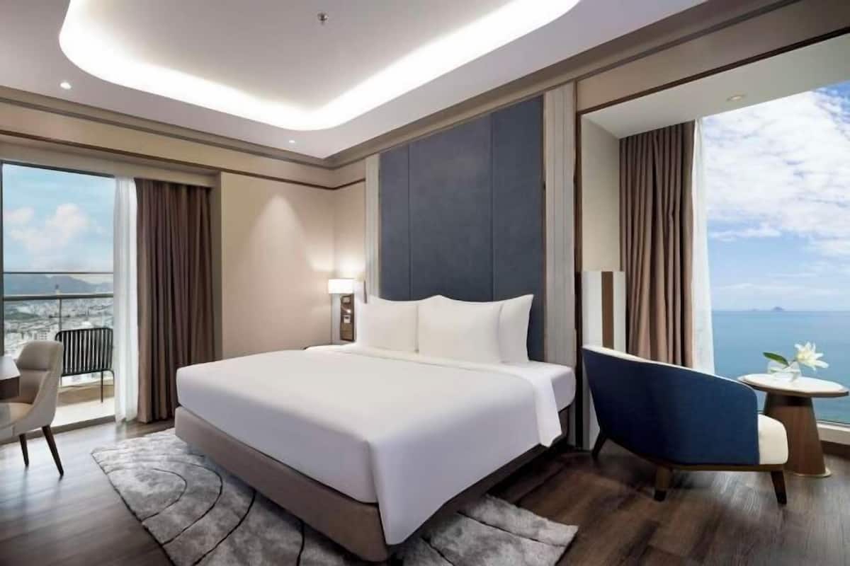 Habitación de hotel moderna con una cama grande, zona de estar y vista al mar.