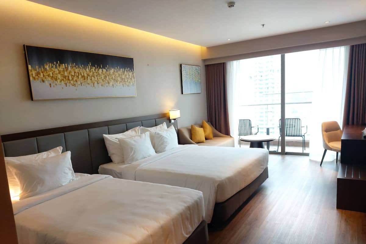 Habitación de hotel con dos camas, un escritorio, una silla y un balcón con vistas.