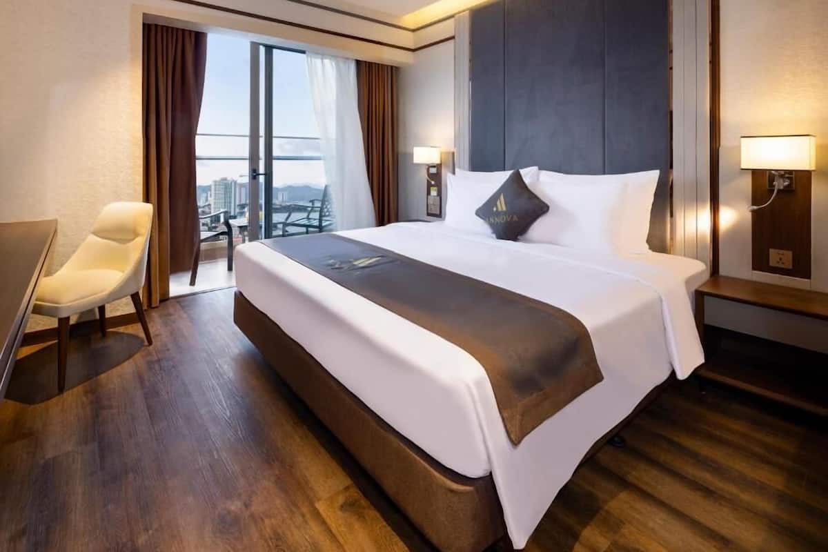Un cuarto de hotel con una cama grande, un escritorio, una silla y vista a la ciudad por la ventana.