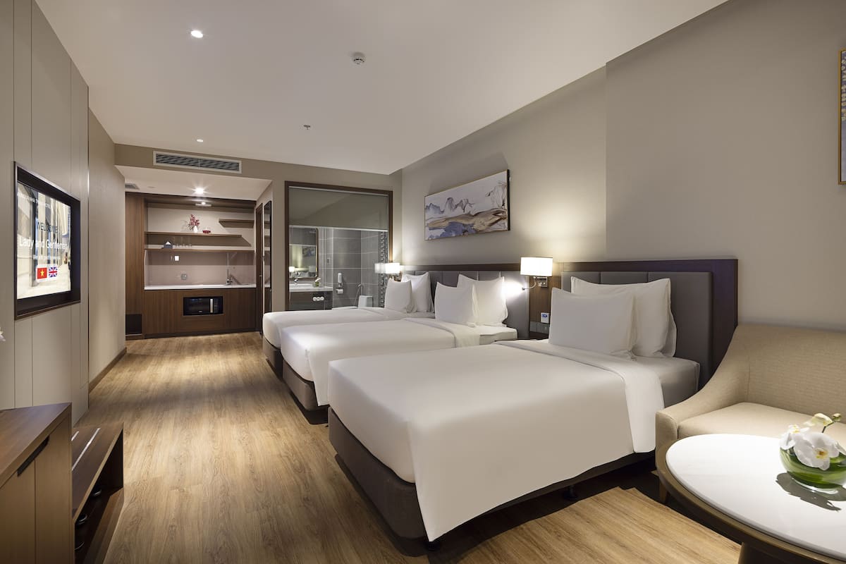 Habitación de hotel con tres camas, zona de estar, baño y un espejo grande.