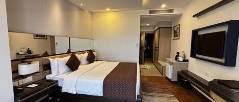 Quarto de hotel com cama, mesas de cabeceira, televisão, espelho e banheiro visível por uma porta aberta.