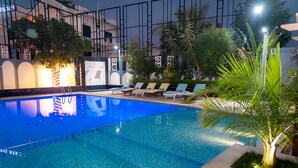 Una piscina con sillones de descanso y una palmera.