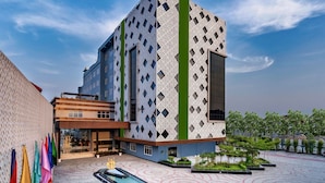 Un edificio moderno con una fachada geométrica distintiva, una franja verde vertical en el centro y un patio con piscina y vegetación.