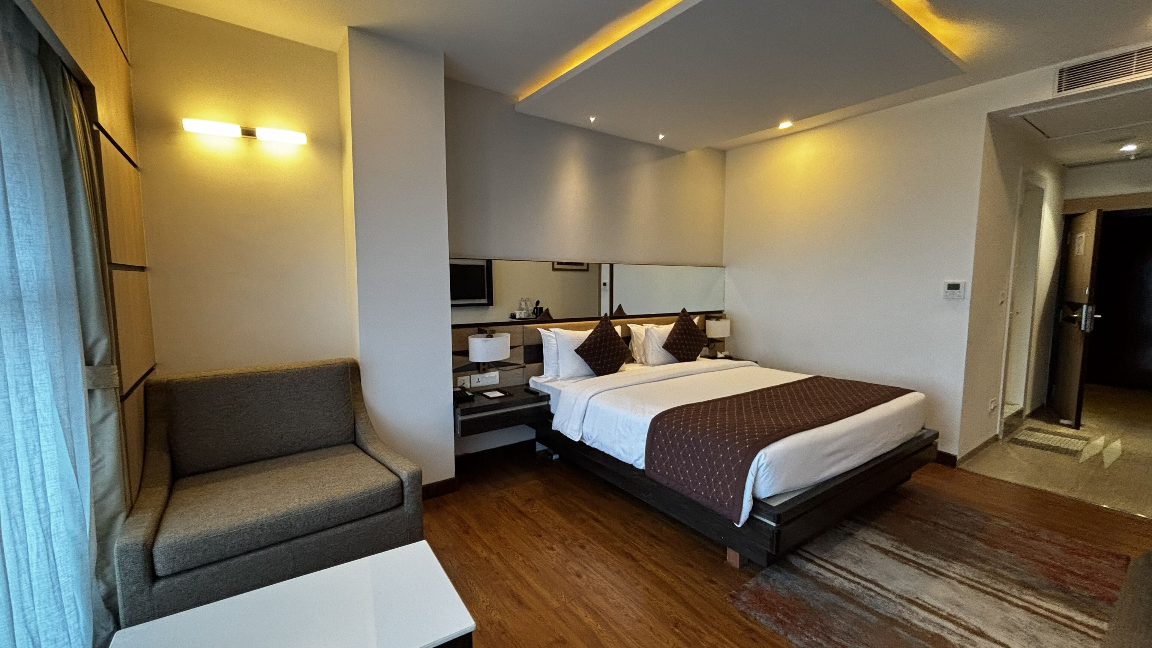 A hotel room with a bed, bedside table, lamp, and a seating area.