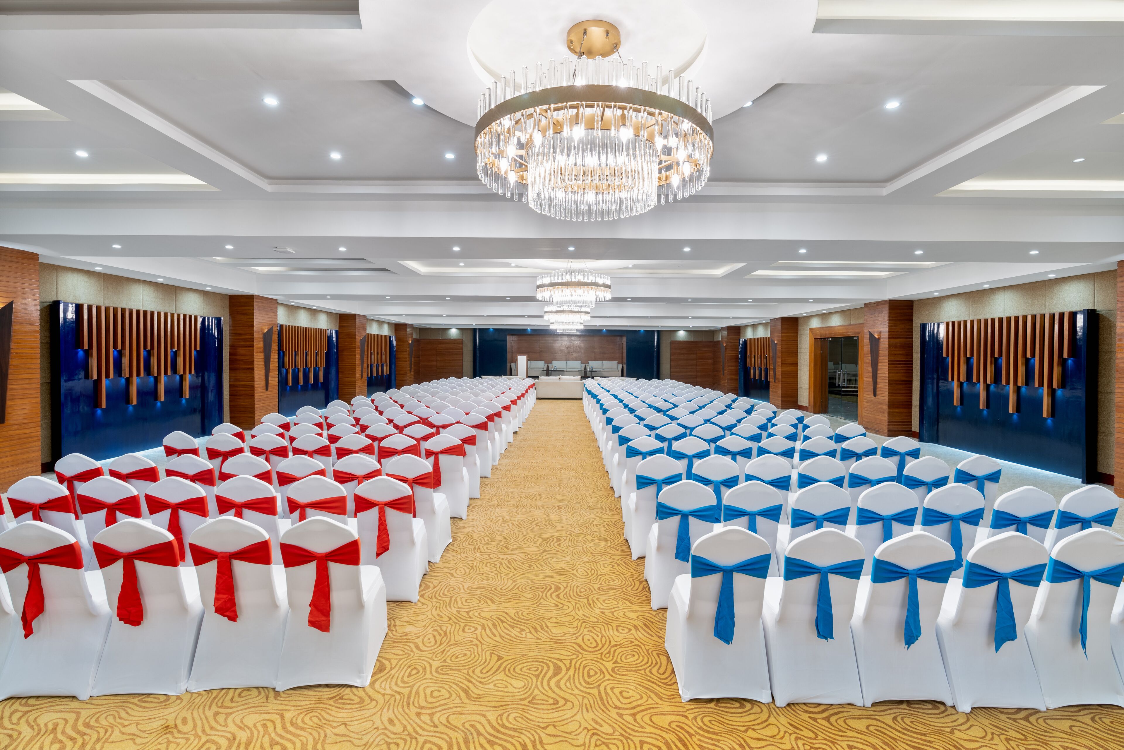 Un salón de banquetes con filas de sillas blancas, cintas rojas y azules, y una gran lámpara de araña.