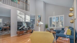 A spacious living room with a sofa, a yellow armchair, and a TV. There is a staircase leading to an upper level. - Super Cute Top Location, Fast WiFi (Reno)