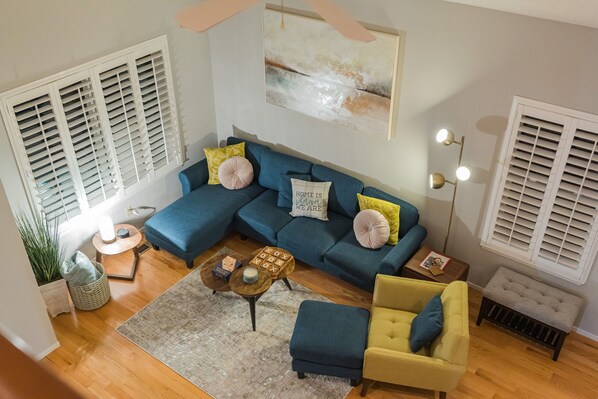 A living room with a blue sectional sofa, a yellow armchair, a coffee table, and a painting on the wall.