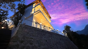 A modern building with a stone base, multiple balconies, and a view of the sky. - Ramshila Cottage (Nainital)