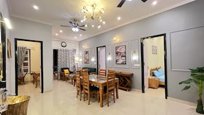 A spacious living area with a dining table, chairs, ceiling fans, and wall-mounted lighting. - Ramshila Cottage (Nainital)