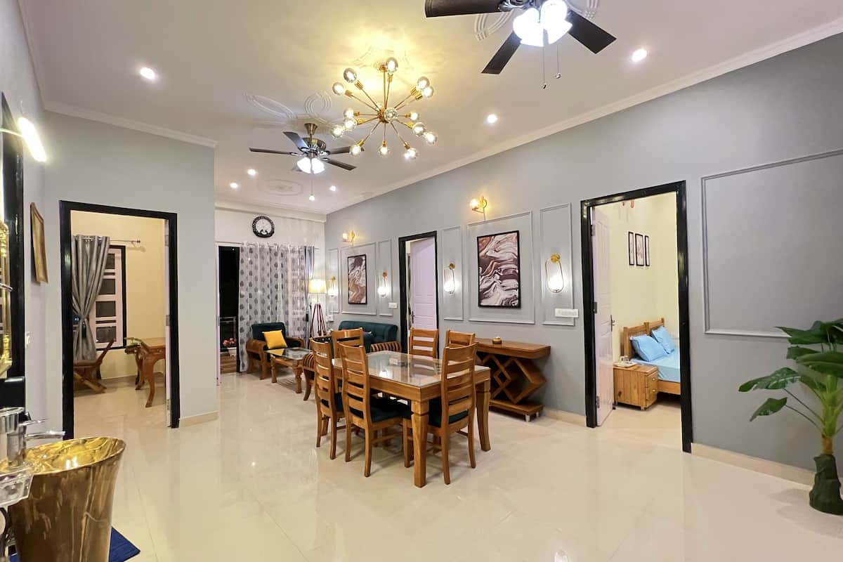 A spacious living area with a dining table, chairs, ceiling fans, and wall-mounted lighting.