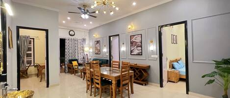 A spacious living area with a dining table, chairs, ceiling fans, and wall-mounted lighting.