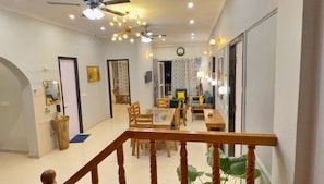 A spacious living area with a dining table, chairs, and a sofa. There is a staircase with a wooden railing leading to an upper floor. - Ramshila Cottage (Nainital)