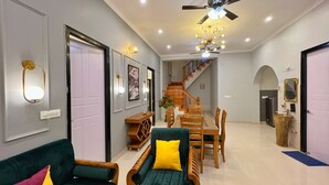 A spacious living area with a green sofa, wooden coffee table, and a dining table with chairs. A staircase leads to an upper floor. - Ramshila Cottage (Nainital)