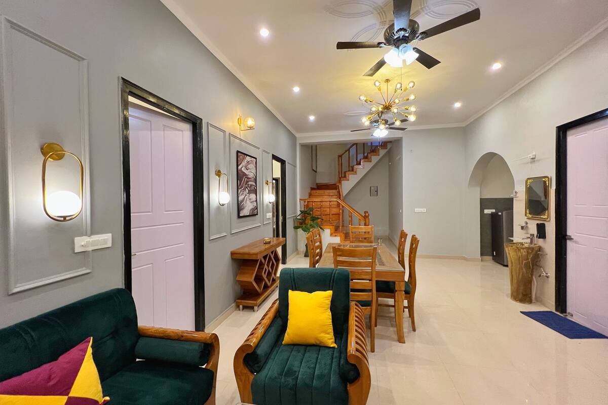 A spacious living area with a green sofa, wooden coffee table, and a dining table with chairs. A staircase leads to an upper floor.