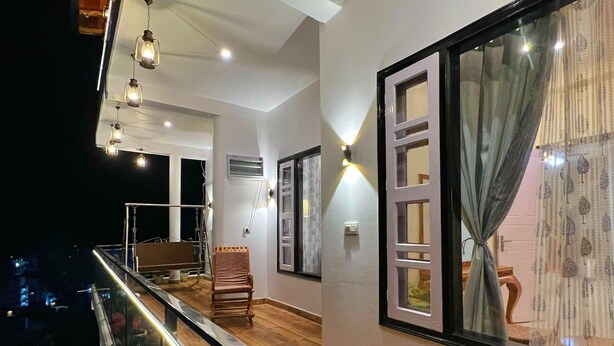 A modern interior with a balcony, wooden flooring, and a view of the city at night. - Ramshila Cottage (Nainital)