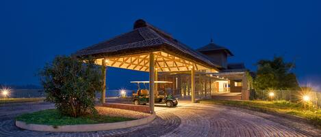 A covered pavilion with a golf cart parked underneath, a brick pathway leading to the entrance, and a building in the background.