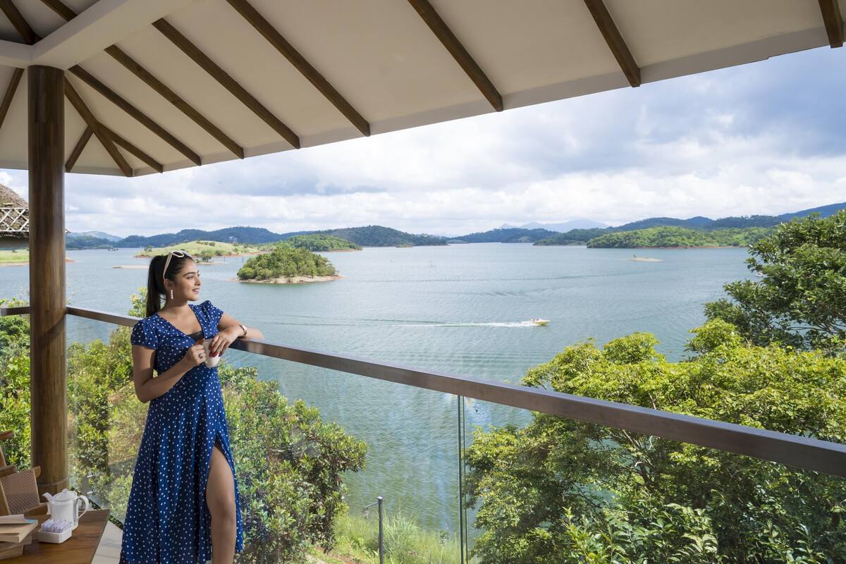 Varanda com vista para um lago, rodeada por vegetação e colinas.