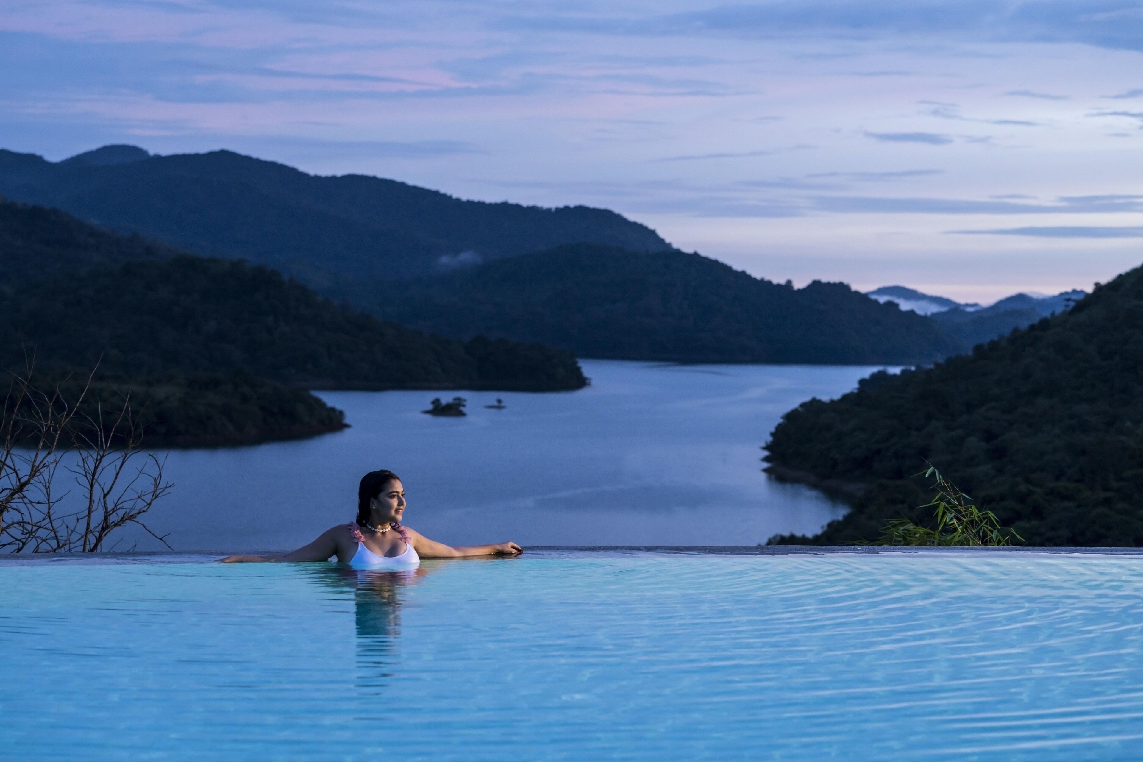 A person in a infinity pool with a view of a lake and mountains.