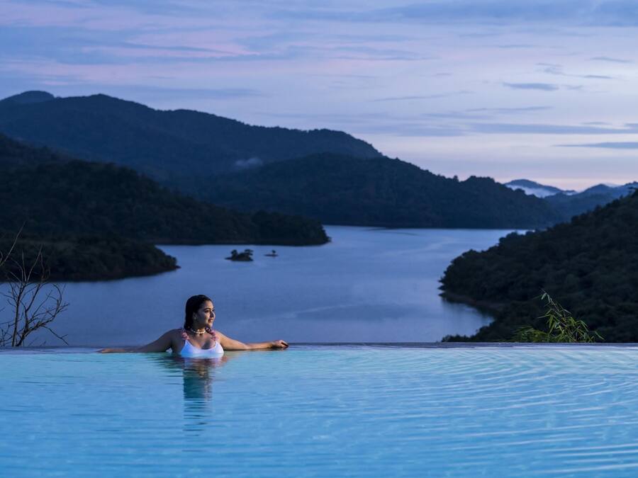 Una persona en una piscina infinita con vistas a un lago y montañas.