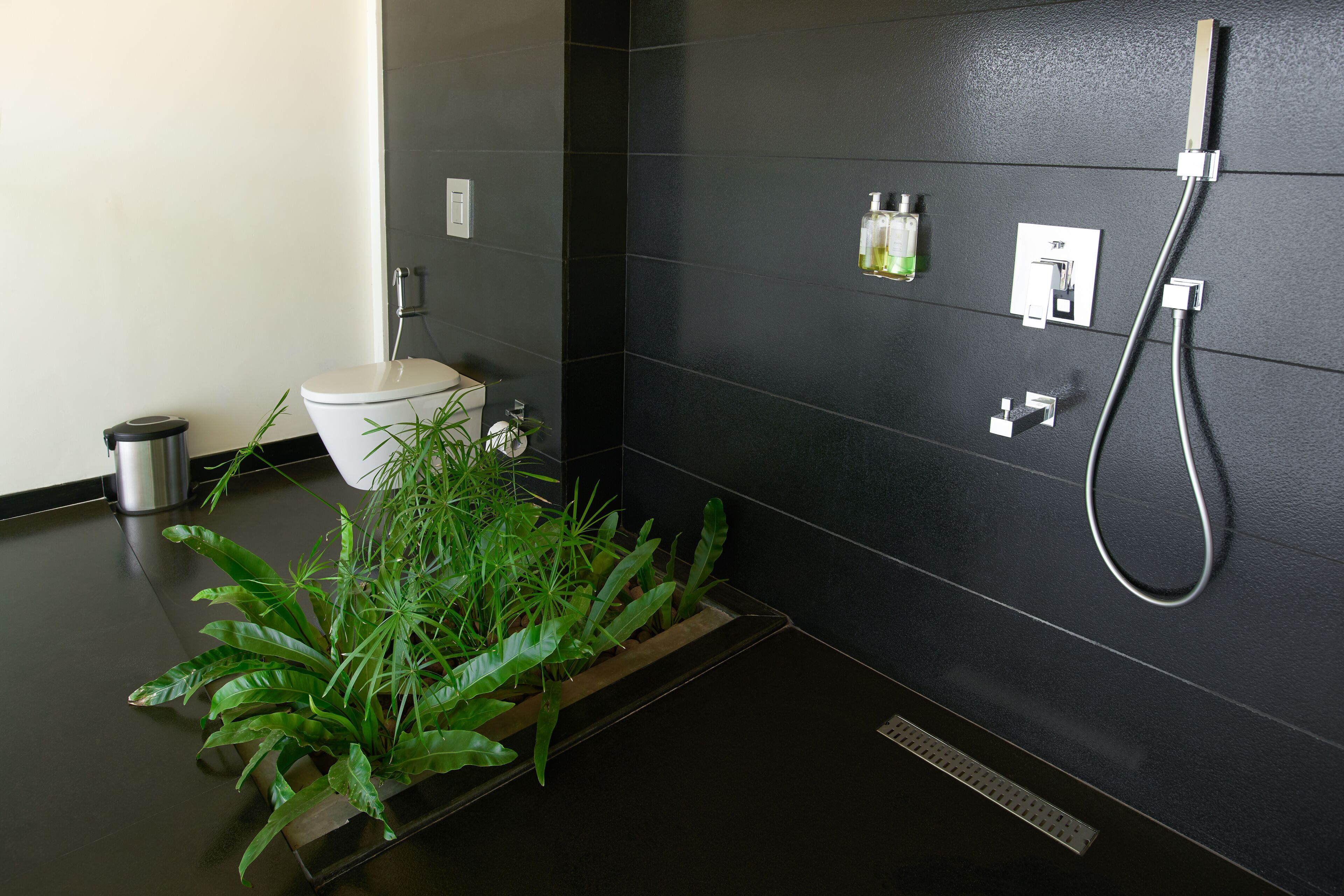 A modern bathroom with a toilet, a shower, and a sink. There are plants on the floor and toiletries on the wall.