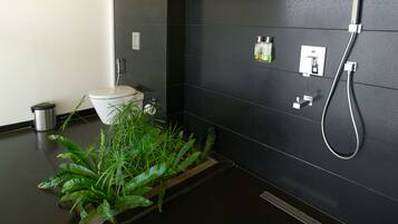 Un baño moderno con inodoro, ducha y lavamanos. Hay plantas en el suelo y artículos de aseo en la pared.